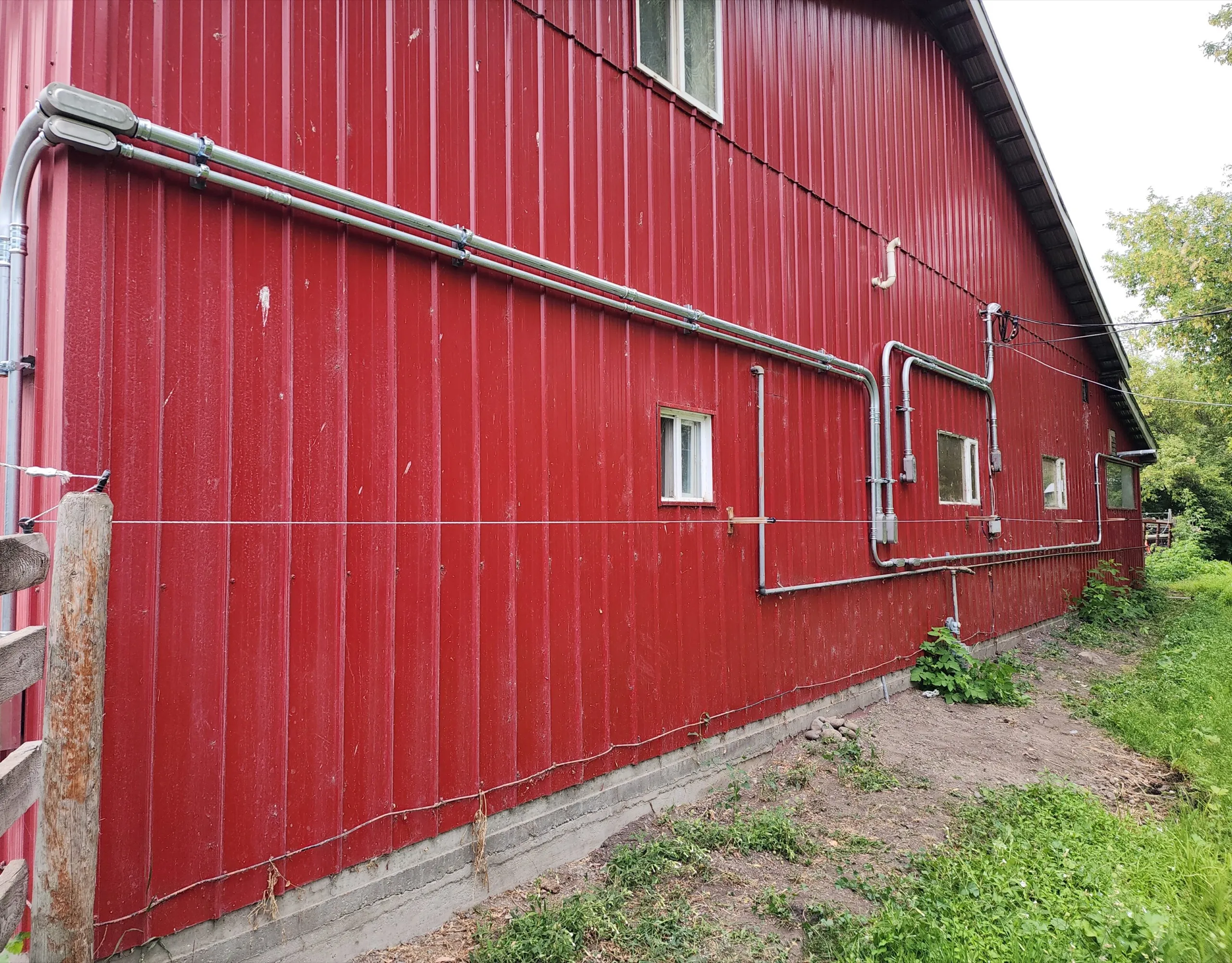 Galvanized conduit runs installed along the exterior of a red agricultural barn
