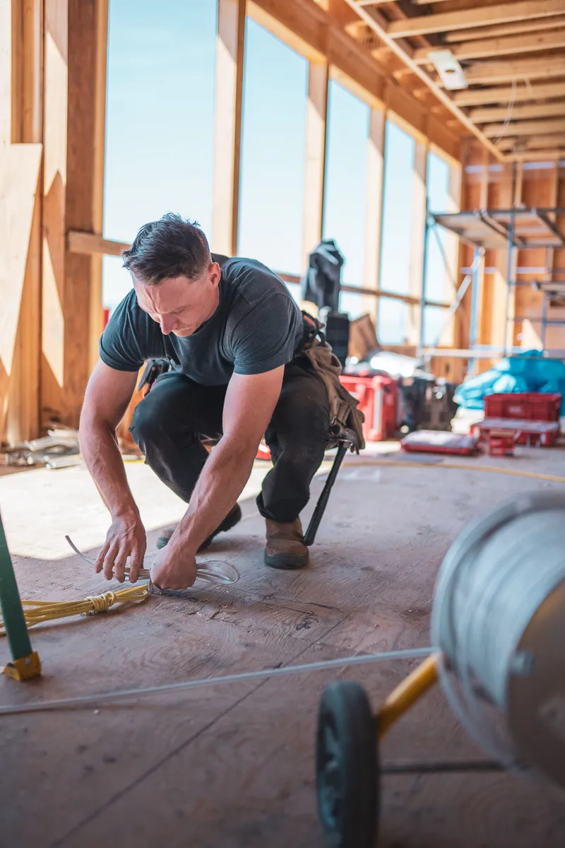 Dayton Power electrician crouching to pull and secure wiring on the floor of a timber-framed building