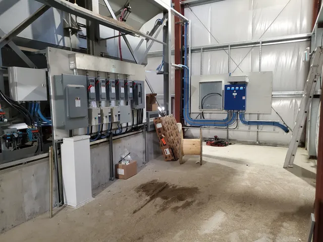 Power distribution wall and conveyor control panel beneath the aggregate bins